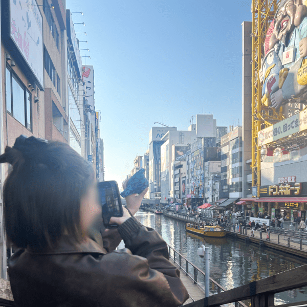 大阪の景色を背景に鳥のぬいぐるみを撮影する様子